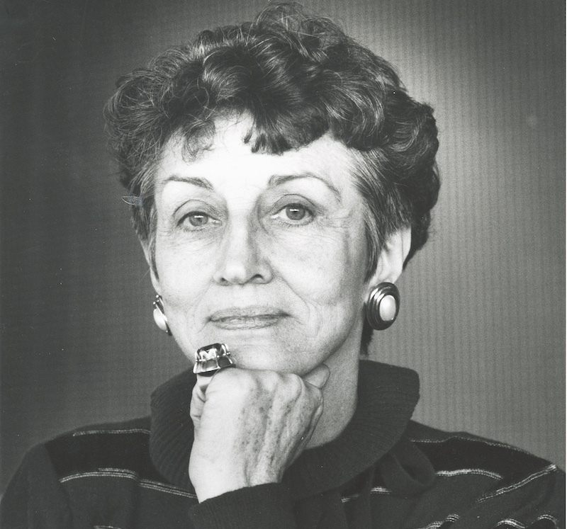 Black and white portrait of a woman with short curly hair and large circular earrings; her left hand, with a large ring, is closed in a fist by her chin